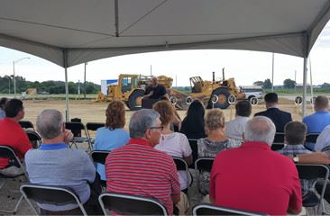 A group of people sitting under a pavilion and construction vehicles in the background
